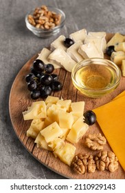 Assorted Cheese On A Wooden Plate On A Gray Background With A Copy Space. Wine Appetizer With Honey, Grapes, Pretzels And Walnuts On A Round Platter. Vertical Orientation, Close-up, No People