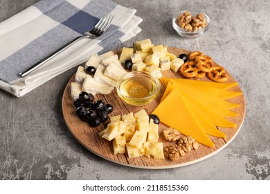 Assorted Cheese On A Wooden Plate On A Gray Background With A Copy Space. Wine Appetizer With Honey, Grapes, Pretzels And Walnuts On A Round Platter. Horizontal Orientation, No People, Copy Space