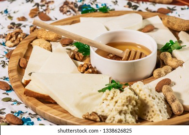 Assorted Cheeses On Round Wooden Board Plate Served With White Wine Guda Cheese, Cheese Grated Bark Of Oak, Hard Cheese Slices, Walnuts, Grapes, Crackers, Honey, Sulguni, Light Wood Background