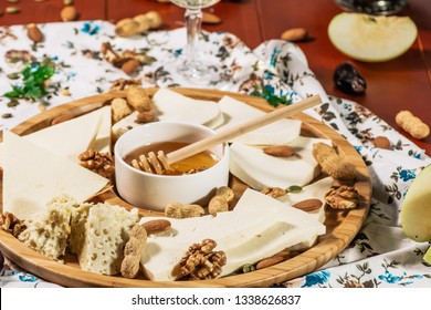 Assorted Cheeses On Round Wooden Board Plate Served With White Wine Guda Cheese, Cheese Grated Bark Of Oak, Hard Cheese Slices, Walnuts, Grapes, Crackers, Honey, Sulguni, Light Wood Background