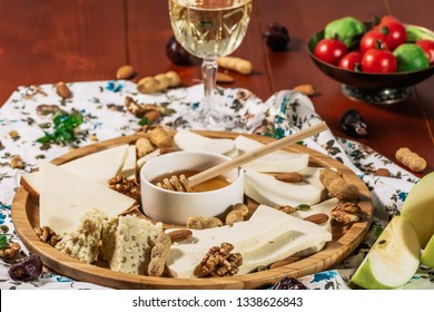 Assorted Cheeses On Round Wooden Board Plate Served With White Wine Guda Cheese, Cheese Grated Bark Of Oak, Hard Cheese Slices, Walnuts, Grapes, Crackers, Honey, Sulguni, Light Wood Background