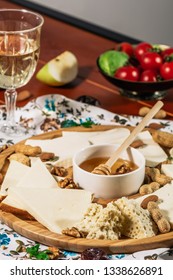 Assorted Cheeses On Round Wooden Board Plate Served With White Wine Guda Cheese, Cheese Grated Bark Of Oak, Hard Cheese Slices, Walnuts, Grapes, Crackers, Honey, Sulguni, Light Wood Background