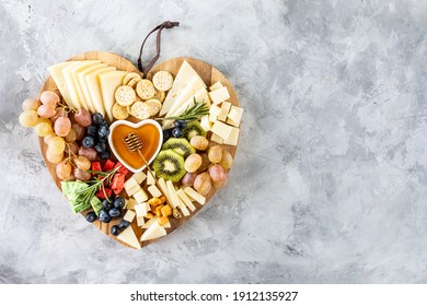 Assorted cheeses on a wooden cutting board in the shape of a heart. Cheese, grapes, walnuts, olives, rosemary and a glass of white wine. top view, copy space - Powered by Shutterstock