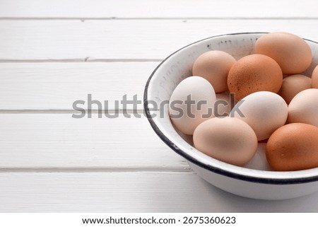 Assorted chicken eggs in different colors placed inside a vintage enamel bowl on a white wooden surface with copy space. Farm fresh, rustic and organic food concept