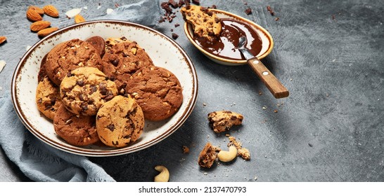 Assorted chocolate chip cookies on wooden plate with cup of coffee on dark background, top view, panorama with copy space.