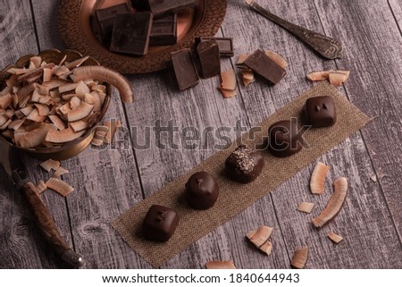 Assorted chocolate handmade praline on dark moody rustic background with dark chocolate chunks and coconut in a shallow background