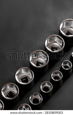 Assorted chrome socket wrench sockets arranged by size on a dark background with clean composition and ample copy space. Diagonal composition.