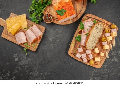 Assorted cold cuts, cheese cubes, bread, and olives on wooden boards with copy space on dark background.