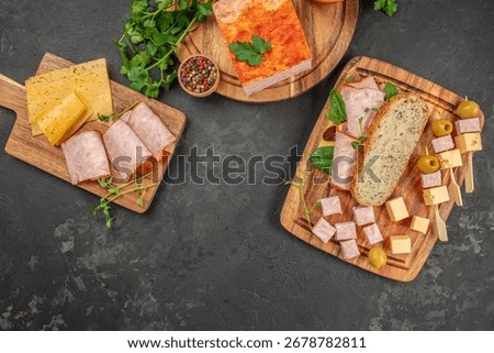 Assorted cold cuts, cheese cubes, bread, and olives on wooden boards with copy space on dark background.