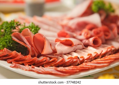 Assorted Cold Cuts (ham, Turkey, Sausage) Arranged On A Plate And Garnished With Fresh Parsley Leaves.