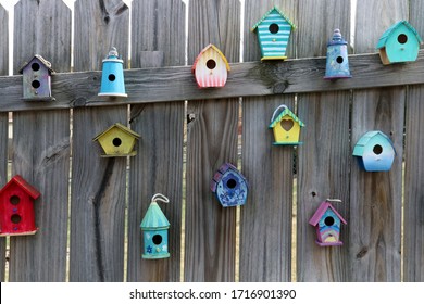 Assorted colored birdhouses hung on wooden fence