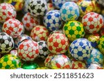 Assorted colorful chocolate candies wrapped in soccer ball patterned foils are seen together. This image depicts a fun and lively scene.