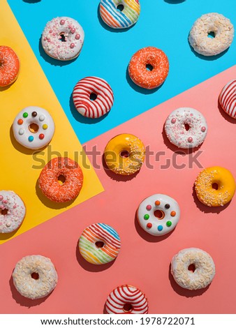 Assorted colorful glazed donuts, top view. Creative layout made from delicious glazed donuts. Vertical flat lay background with multicolored donuts or doughnuts. Blue yellow pink backdrop. Hard light