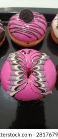 Assorted colorful glazed donuts with various toppings arranged on a black baking tray.