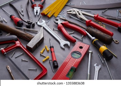 Assorted Colorful Red Hand Tools For Building And Construction Mixed With A Vintage Hand Saw, Snips And Mallet On Grey Viewed Full Frame High Angle