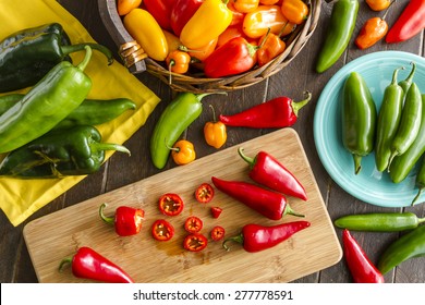 Assorted colorful varieties of hot and sweet peppers sitting on table with cutting board, yellowe napkin and blue plate - Powered by Shutterstock