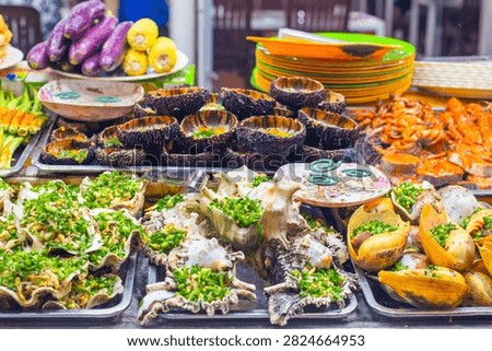 Assorted cooked seafood dishes including sea urchins and scallops at a street food market stall. Asian seafood dining.