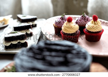 Assorted desserts on a table, featuring chocolate cake slices and red velvet cupcakes with cream frosting and raspberries.
