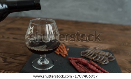 Assorted different types of jerky meat on black stone plate. Wine snacks with red wine in glass. Small sausages, meat delicatessen. Friday night taproom party atmosphere craft brewery concept.