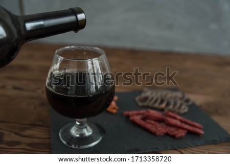Assorted different types of jerky meat on black stone plate. Wine snacks with red wine in glass. Small sausages, meat delicatessen. Friday night taproom party atmosphere craft brewery concept.