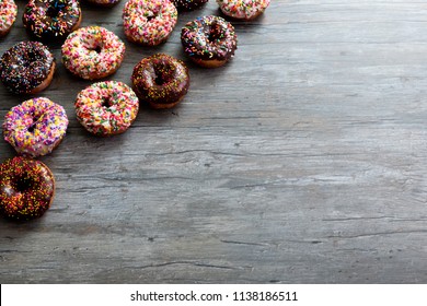 Assorted Donuts on wood background, top down, layout, copy space, blank space. Chocolate and vanilla frosted doughnuts with colorful sprinkles. Glazed donuts with sprinkles wood background. 