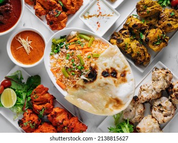 Assorted famous indian and pakistani food table vegetable biryani, Butter Chicken, paneer Chicken Tikka boti kebab, lime, Kali Mirchi, tomato sauce, raita, roti, salad, top view on grey background