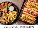 Assorted fast food items including hot dogs, chicken strips, and fries on a platter with dipping sauces. Perfect for a casual meal or party snack.