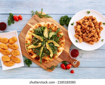 Assorted fastfood Avocado Rockets Pizza, Crispy Nuggets With BBQ Dips, Popcorn Chicken Served in dish isolated on wooden table top view fastfood