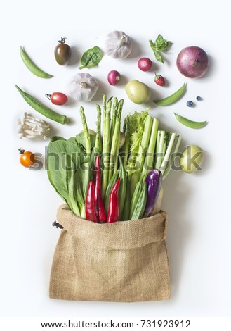 Assorted flat lay colourful uncooked vegetables in traditional hessian sack on white background.