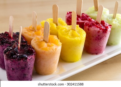 Assorted Flavors Of Homemade Fresh Pureed Frozen Fruit Popsicles Sitting On White Plate In A Row