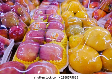 Assorted fresh fruits at market stall display wrapped in plastic film wrap for protection. The plastic wrappers are wasteful and unsustainable for the environment