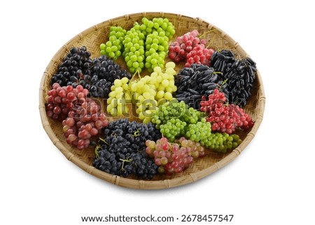 Assorted fresh grape varieties in a woven bamboo basket, featuring red, green, black, and elongated grapes on white background.