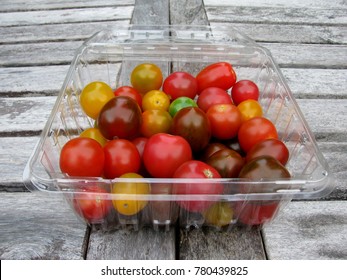 Assorted fresh organic colorful tomatoes in a plastic container on a wooden table - Powered by Shutterstock