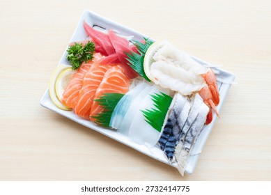 Assorted fresh sashimi platter featuring salmon, tuna, squid, shrimp, and mackerel. Premium Japanese seafood served on a white plate, top view.