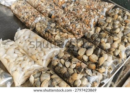 Assorted fresh shellfish and seafood packaged in transparent plastic bags filled with water at a local seafood market. Represents seafood trade, freshness and traditional market culture.