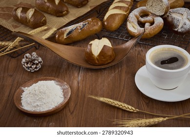 Assorted freshly baked bread rolls with flour, wheat ears, and a cup of coffee on a rustic wooden table.