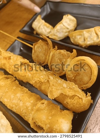 Assorted fried snacks and dumplings served on black plates at a casual dining restaurant.