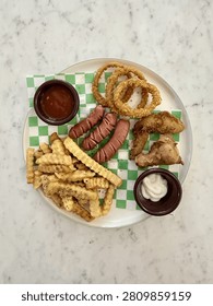 Assorted fried snacks served on a plate with dipping sauces on a marble table, top view.