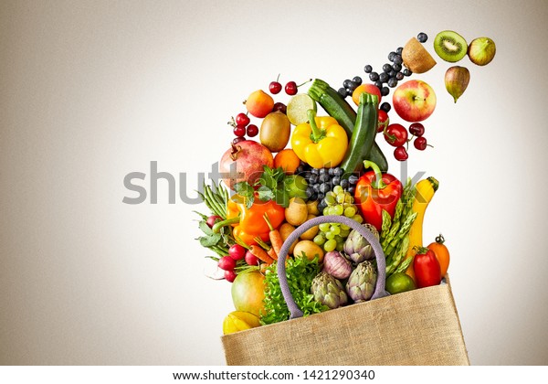 Assorted fruits including bananas and kiwifruits in pile of vegetables spilled out from canvas grocery bag