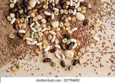 Assorted garden seeds scattered over burlap on rustic wood background.  Seeds include various beans, peas, corn, radishes, and carrots.