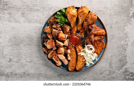 Assorted grilled meat in a plate on the table top view. Fried chicken legs and wings, sausages, shish kebab, pickled onions and tomato sauce. Horizontal orientation, copy space, no people
