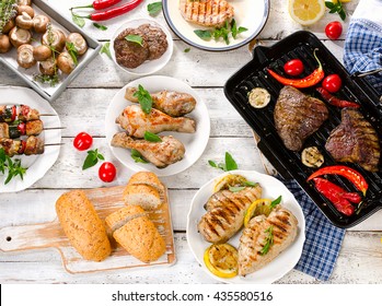 Assorted grilled meat with vegetable on a white wooden table. Top view