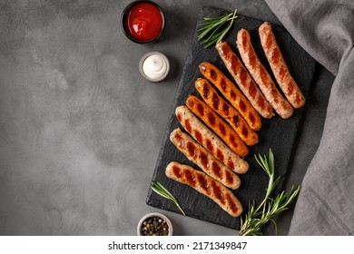 Assorted grilled sausages on barbecue with sauces. Assortment of different sausages on slate board and dark background. Top view, copy space.