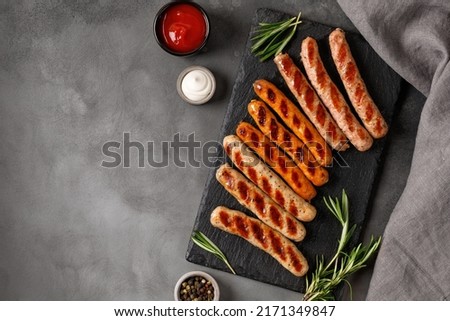 Assorted grilled sausages on barbecue with sauces. Assortment of different sausages on slate board and dark background. Top view, copy space.