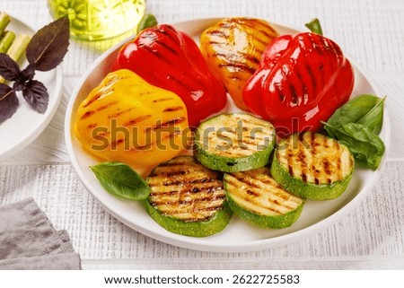 Assorted grilled vegetables including bell peppers, zucchini, and fresh herbs arranged on a rustic wooden table, captured in a vibrant flat lay composition