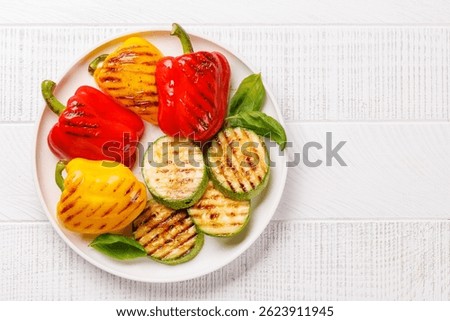 Assorted grilled vegetables including bell peppers, zucchini, and fresh herbs arranged on a rustic wooden table, captured in a vibrant flat lay composition