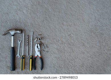 Assorted hand tools arranged on a textured concrete surface, representing DIY repair, craftsmanship, and home maintenance. A practical flat‑lay featuring a hammer, screwdrivers, pliers, wrench, drill bit, screws, and metal sockets on a rugged grey background. Perfect for themes of construction, handyman work, mechanical repair, tool kits, Father’s Day promotions, and home improvement projects