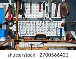 Assorted hand tools hanging on wall-mounted pegboard in workshop, including wrenches, pliers, hammers, screwdrivers, power strip and various hardware supplies arranged on workbench