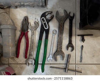 Assorted Hand Tools Including Wrenches, Pliers, and Pipe Fittings on a Tiled Surface