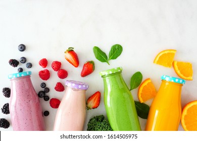 Assorted healthy fruit smoothies in bottles with ingredients. Top view against a white marble background. Blueberry, strawberry, green and orange.